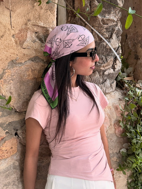 Woman wearing a pink headscarf and sunglasses against a stone wall.