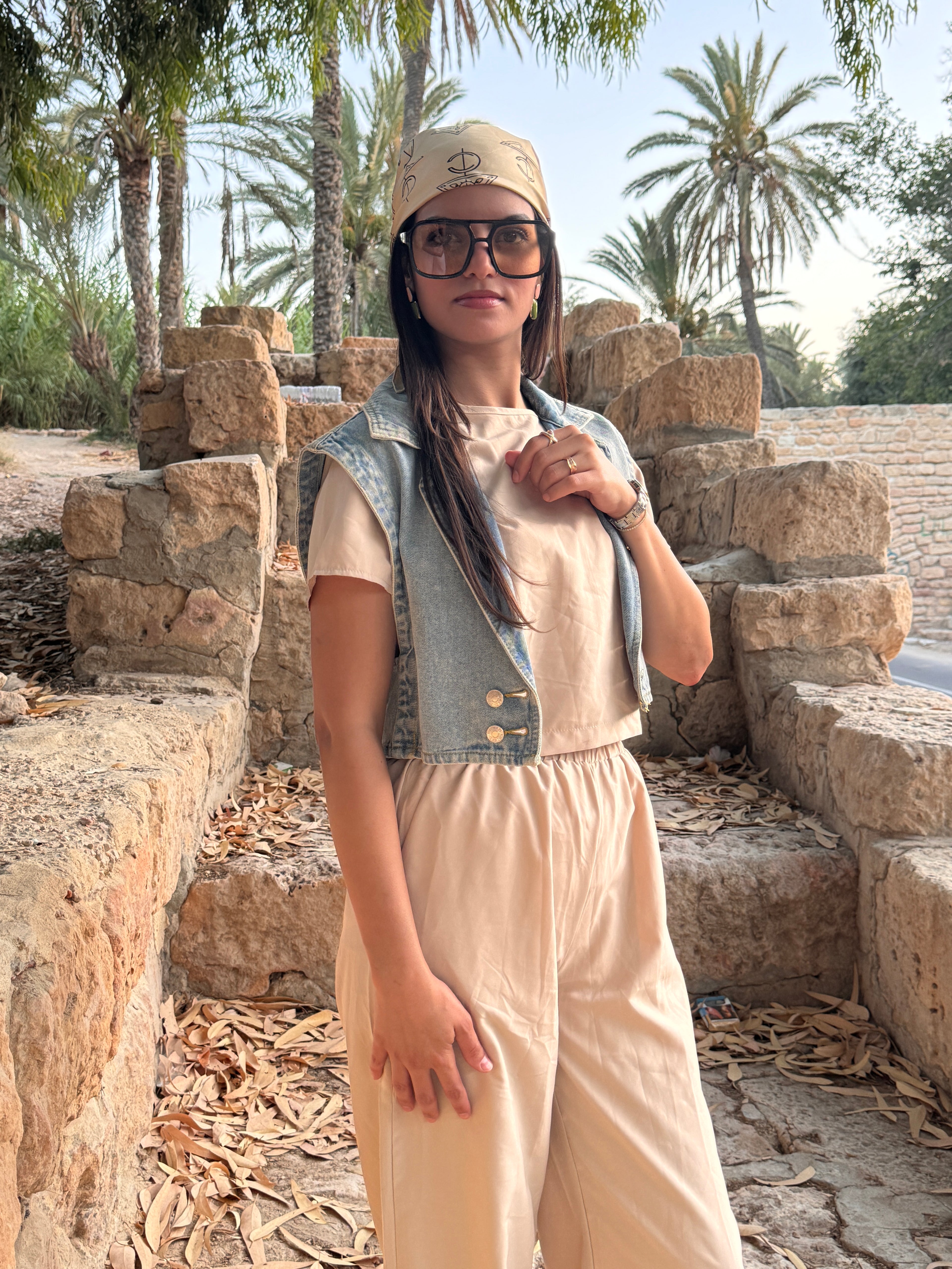 Person standing outdoors with palm trees and stone architecture in the background